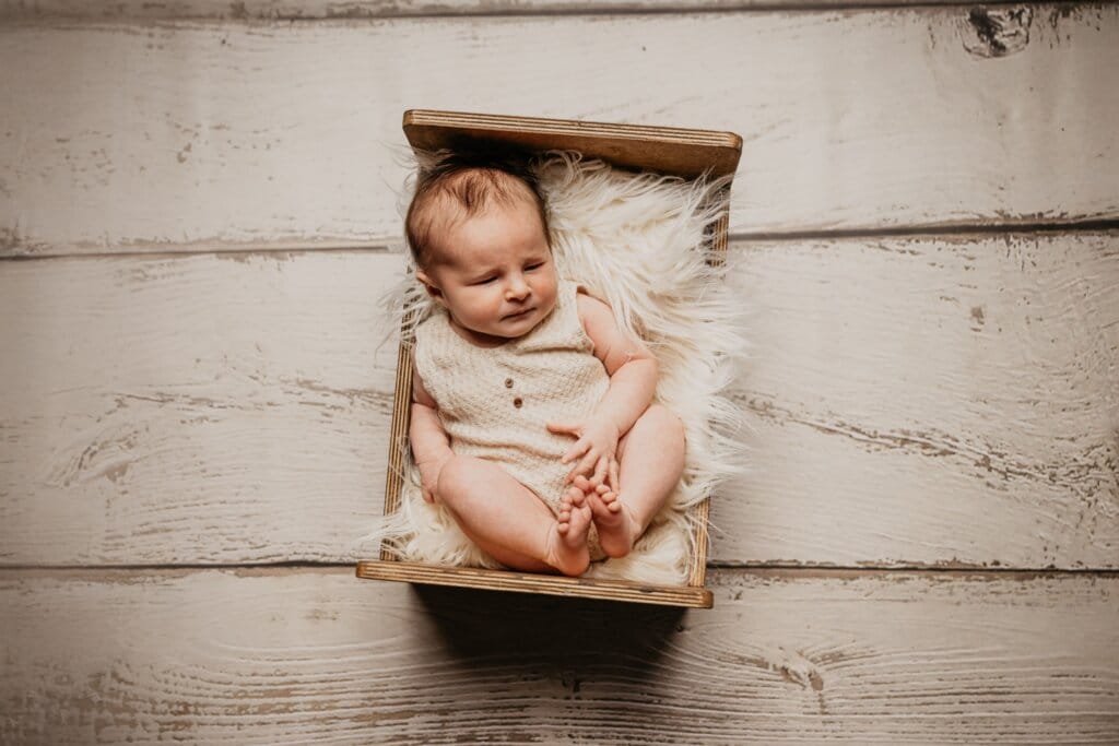 Bébé nouveau-né photographié à Rennes sur un support en bois dans un style naturel et minimaliste.